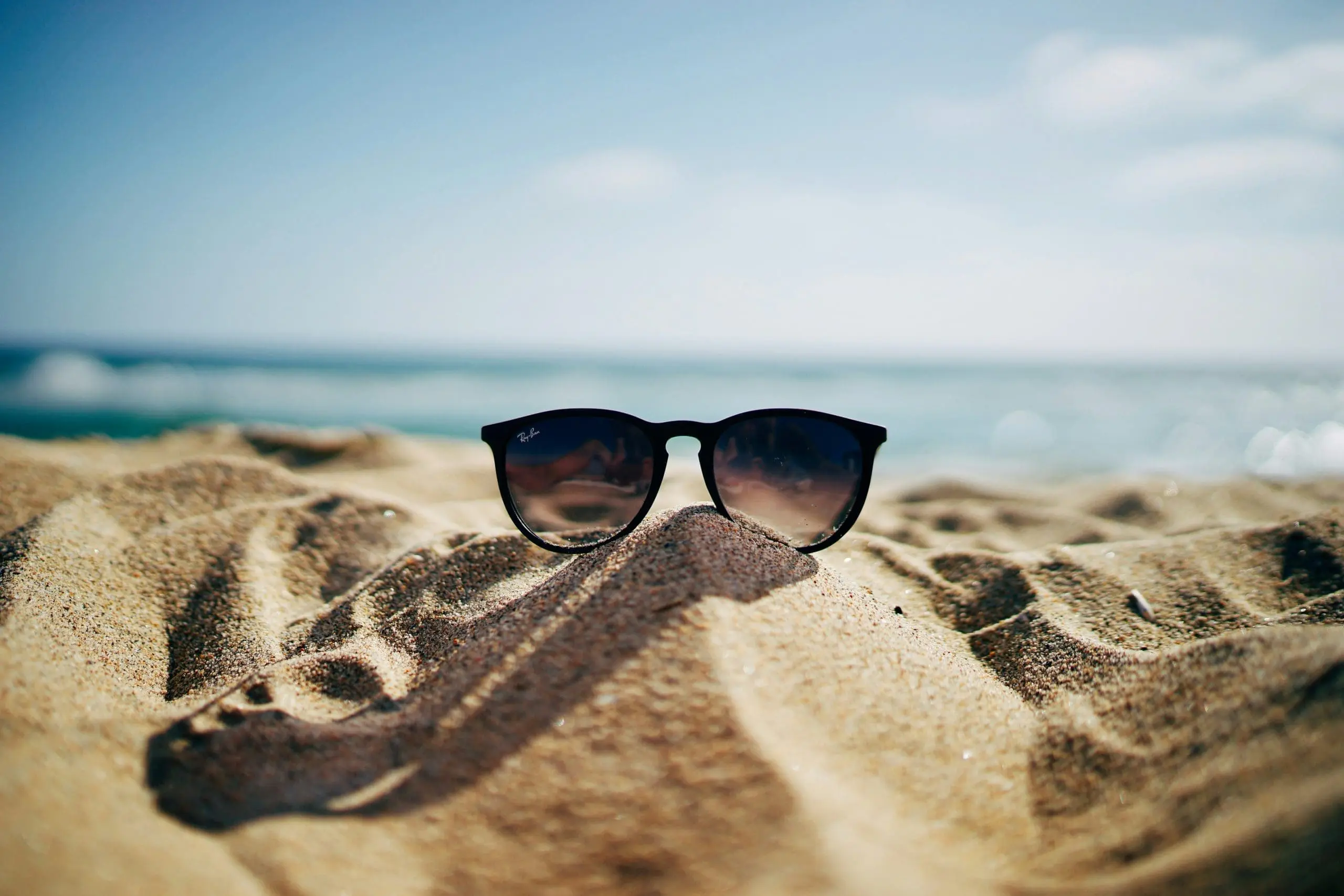 Black sunglasses resting on a sandy beach with the sea and sky in the background
